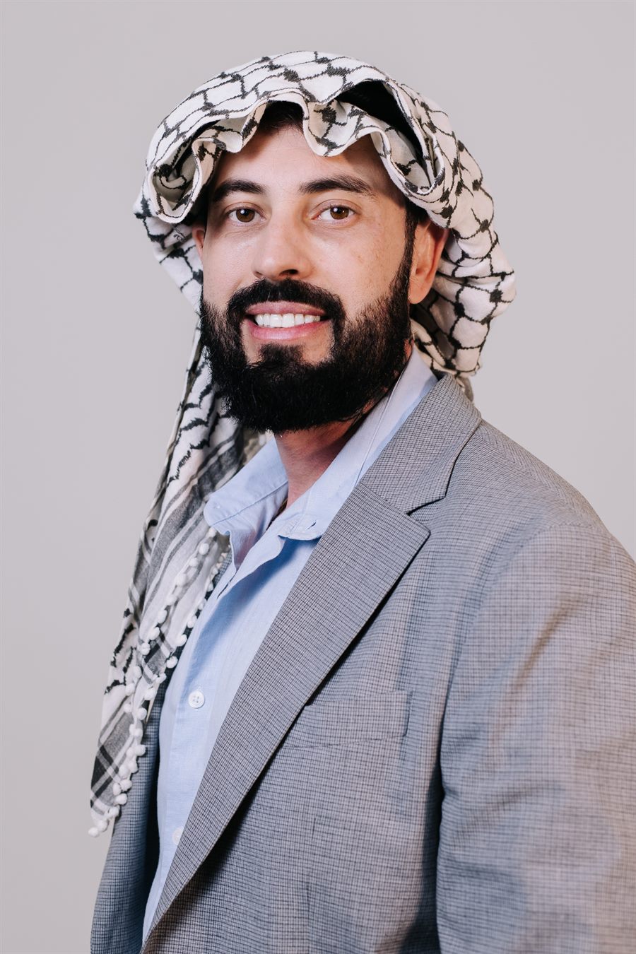 Delegado Yasser sorrindo, vestindo o kufiya palestino sobre o blazer